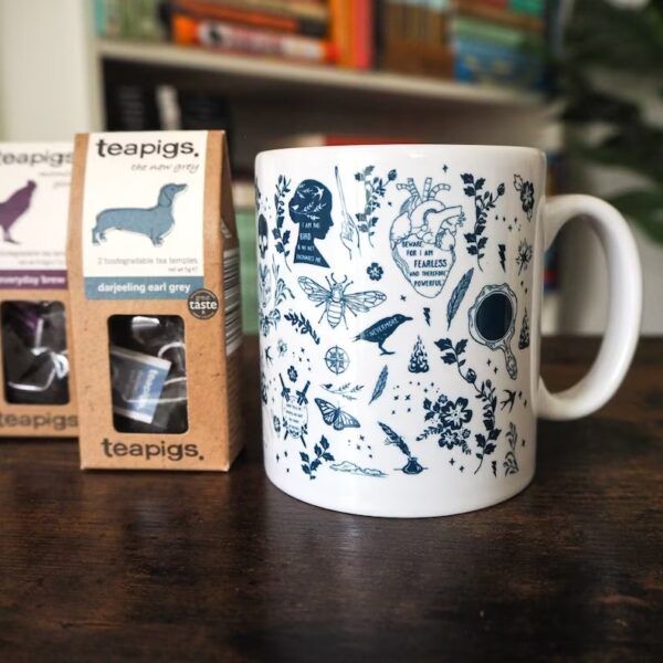 Mug en céramique blanche avec des dessins littéraires en bleu et des sachets de thé sur le côté.
